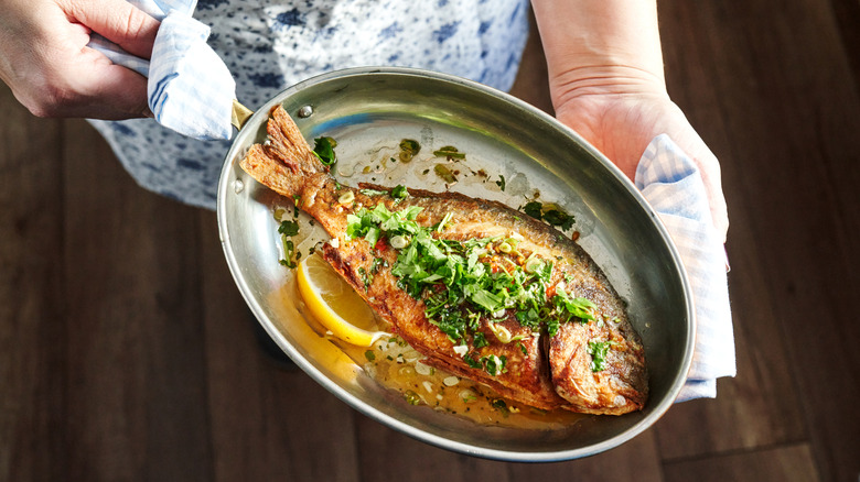 Une femme tenant une poêle de fruits de mer grillés avec des tranches de citron et une garniture