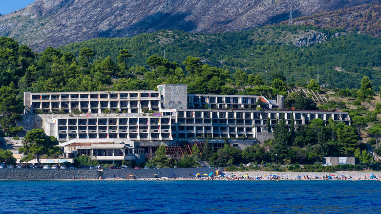 Un grand hôtel abandonné entouré de verdure au pied d’une montagne