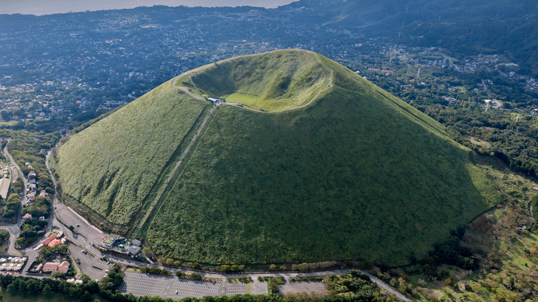 Le cratère d'un volcan recouvert d'herbe avec un paysage urbain en arrière-plan