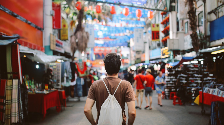 Vue arrière d'un homme avec un sac à bandoulière face à une rue malaisienne avec des boutiques et des banderoles festives au-dessus