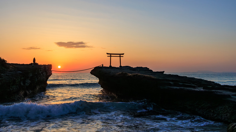 Silhouette d'un torii se dresse sur un rocher en mer au coucher du soleil à Shimoda, Japon