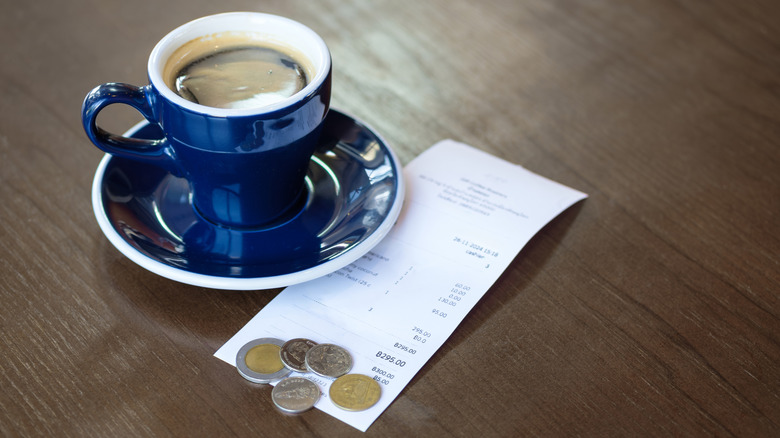 Une petite tasse de café bleue avec des pièces en euros et un reçu sur la table