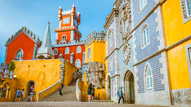 L'entrée du palais de Pena, mettant en valeur les couleurs vives, les carreaux bleus et quelques touristes marchant sur une petite place et montant les escaliers