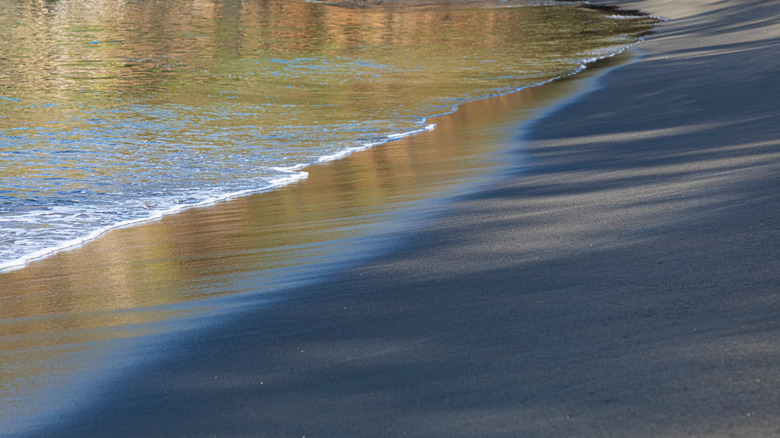 Une vague échouée sur le rivage de sable noir du mont. Wynne Beach