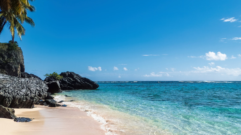 Rochers noirs et sable blanc sur une plage aux eaux cristallines