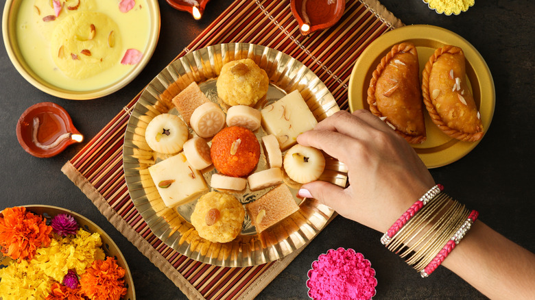 Gros plan sur la main et le bras d'une femme, ornés d'élégants bracelets, enlevant des bonbons Diwali d'une assiette partagée en Inde