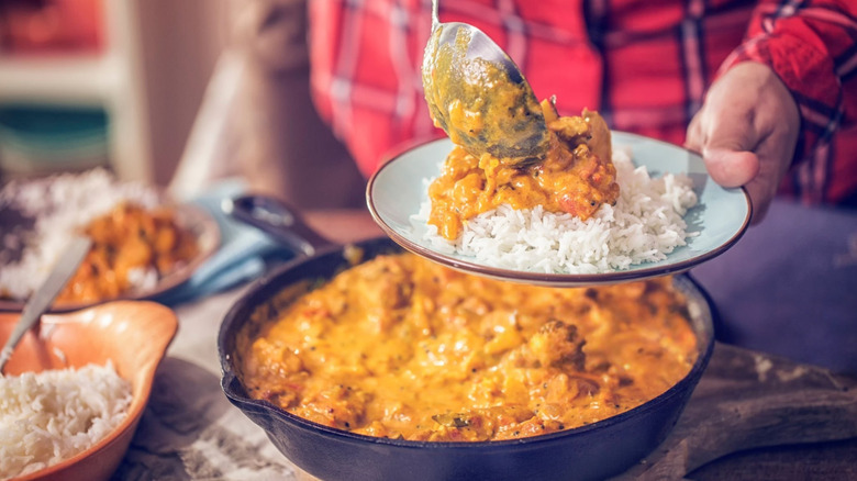 Un homme vêtu d'une chemise à carreaux rouge sert du curry chaud à l'indienne sur du riz fumant dans une assiette avec une grande cuillère de service en métal